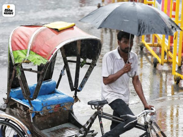लखनऊ में बारिश के बीच छतरी तानकर जाता रिक्शा चालक।