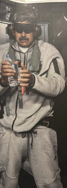 US President Trump posted a picture of Maduro on social media. In the photo, Maduro is wearing a grey Nike tracksuit. He is holding a water bottle in his hand, which is in handcuffs. His eyes are covered with a black strip, and he is wearing headphones.
