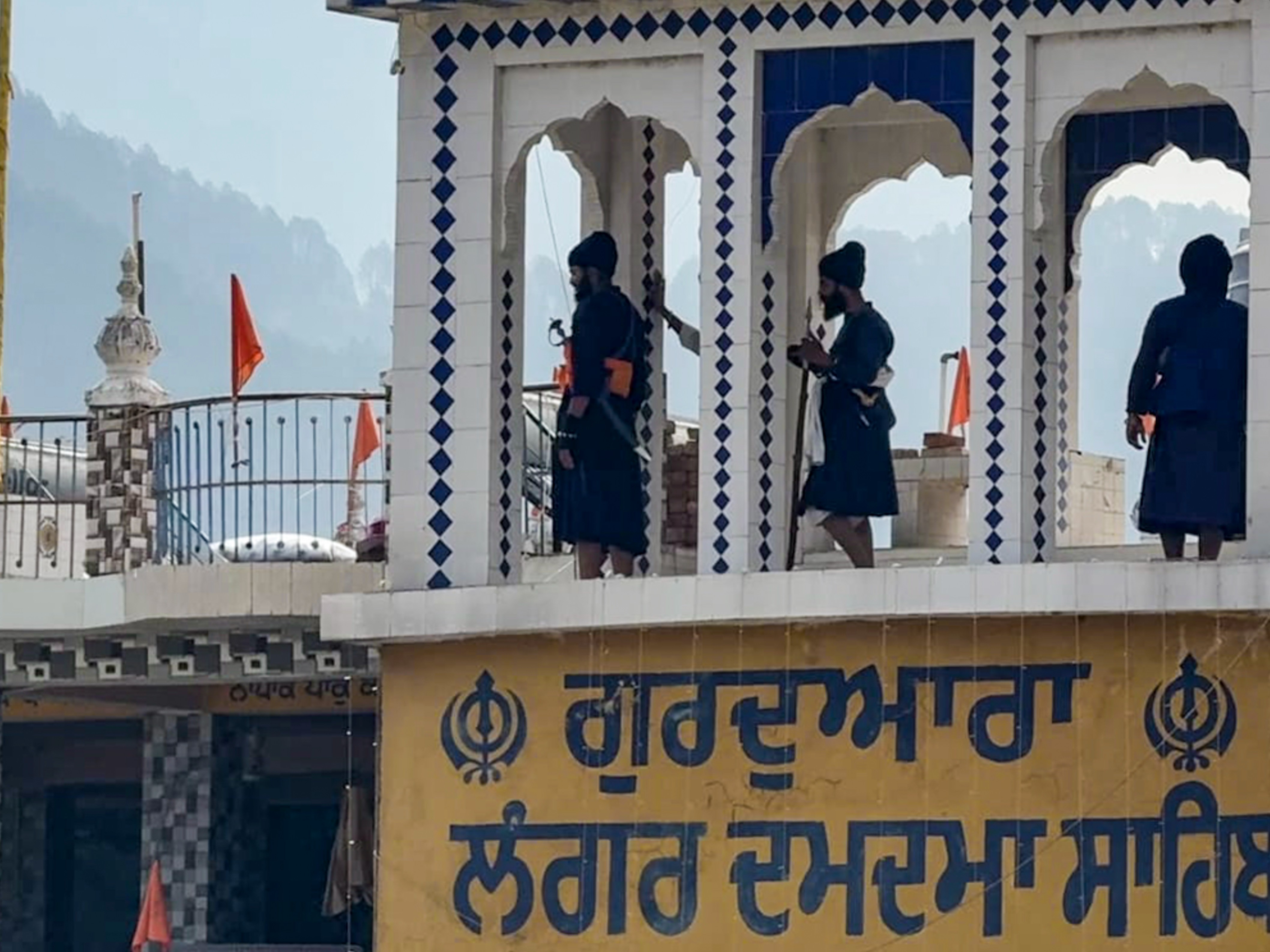 रुद्रप्रयाग: उत्तराखंड के रुद्रप्रयाग में ''निहंग'' चमोली जिले में झड़प के बाद गिरफ्तार किए गए सिख संप्रदाय के चार सदस्यों की रिहाई की मांग को लेकर गुरुद्वारे की छत पर खड़े हैं। (छवि स्रोत: पीटीआई फोटो) - भास्कर इंग्लिश