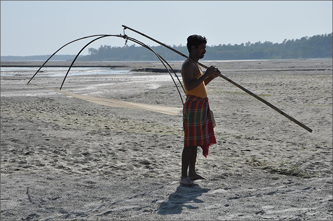 A fisherman in Mekhligunj, West Bengal, stands on the dry bed of the Teesta River holding a net designed for use in shallow waters. (Photo: ORF, 2016)