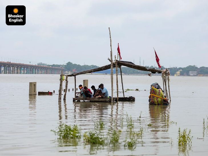 People sit on a partially submerged wooden platform beneath a temporary shelter as the water level of the Ganga and Yamuna rivers rises at Sangam after continuous heavy monsoon rain, in Prayagraj.