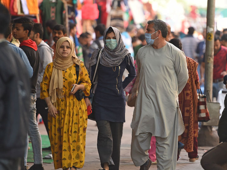 दिल्ली के एक व्यस्त इलाके में मास्क लगाकर जाते लोग।