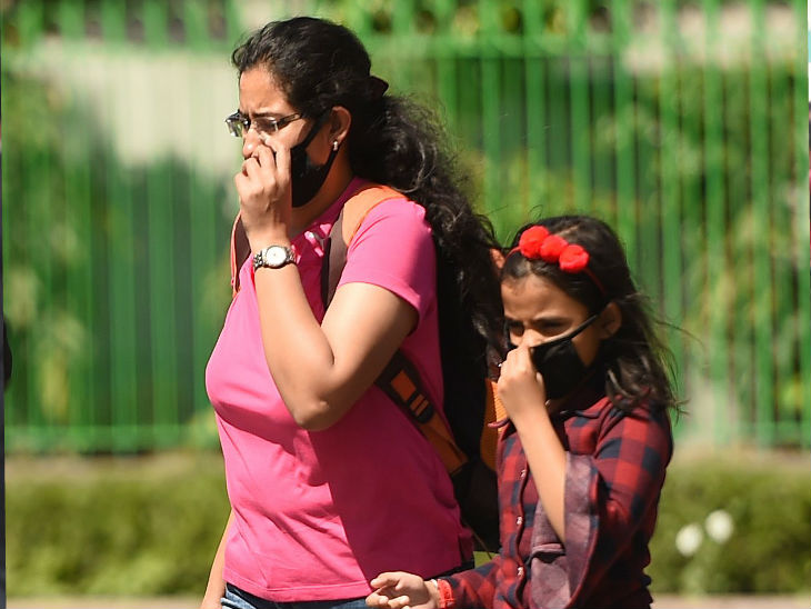 दिल्ली में मास्क लगाकर अपनी बच्ची के साथ जाती एक महिला।