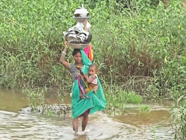 बच्चे को गोद में लेकर नाला पार कर रही महिला