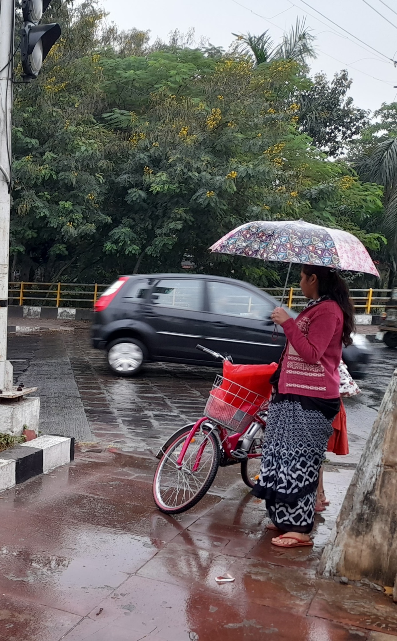 भोपाल के लिंक रोड नंबर-1 पर बारिश के दौरान महिला छतरी से सामान को बचाती हुई।