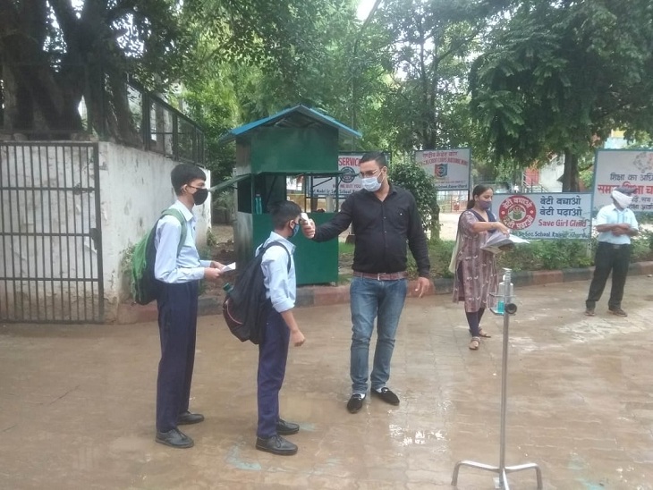 स्कूल पहुंचे बच्चों का तापमान चेक करते स्टाफ के सदस्य।