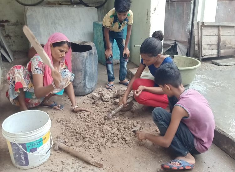 सूखी मिट्टी को तोड़कर उससे गिली मिट्टी बनाते हुए नाथीदेवी व बच्चे।