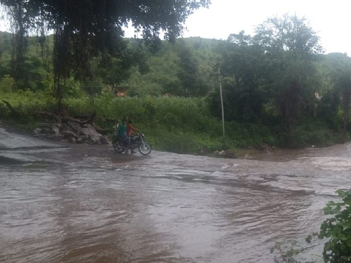 उदयपुर जिले में तेज बारिश के बाद बरसाती नाले में बहते पानी के बीच से गुजरते मोटर साइकिल सवार युवक।
