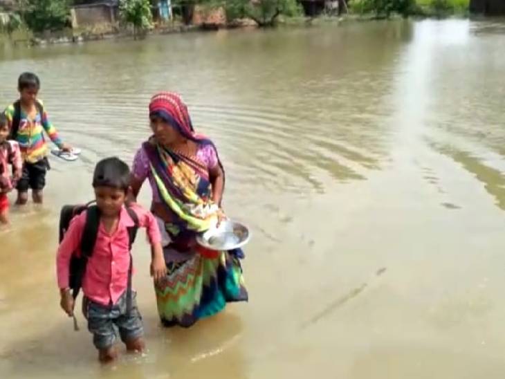 पानी के बीच बच्चों को स्कूल छोड़ने जाते उनके परिजन।