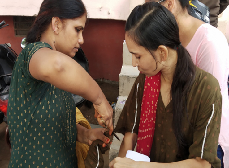 परीक्षा केंद्र के बाहर रखी कैंची से एक अभ्यर्थी के सूट की आस्तीन काटने में मदद करती दूसरी अभ्यर्थी।