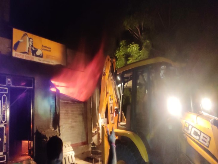 जेसीबी से दुकान का शटर तोड़ते हुए। दुकान के अंदर लगी आग।