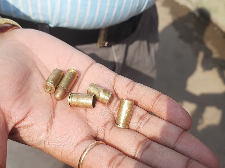 घर के बाहर मिले गोलियों के खोल दिखाते पुलिस कर्मी।