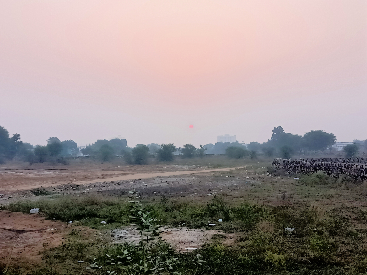 खेतों में धुंध और आसमान पर लाल बंदी जैसा नजर आता सूरज।