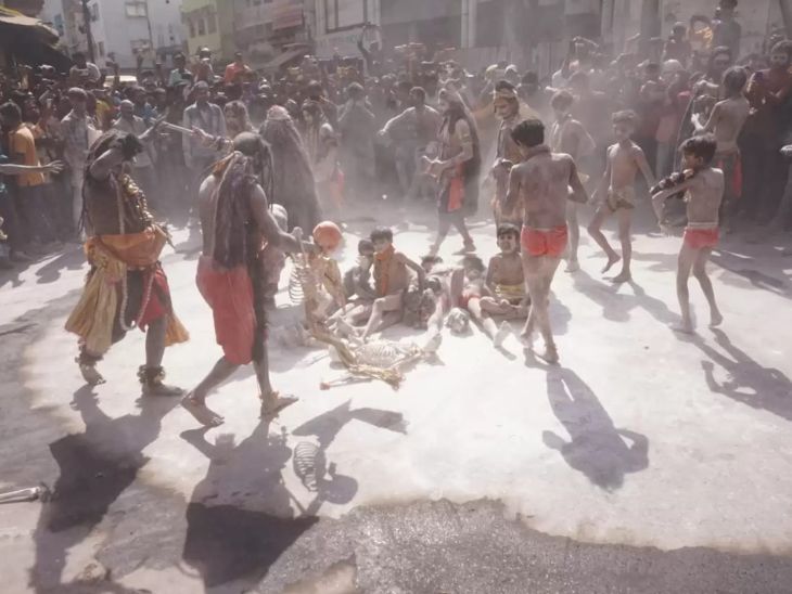 राख के ऊपर बैठकर होली खेलते शिव भक्त। आस-पास बड़ी संख्या में लोग मौजूद हैं।