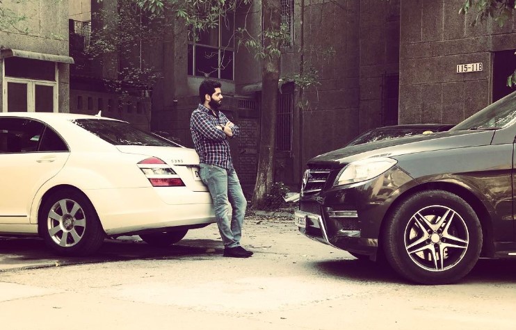 Umar is standing with luxury vehicles in the photo.