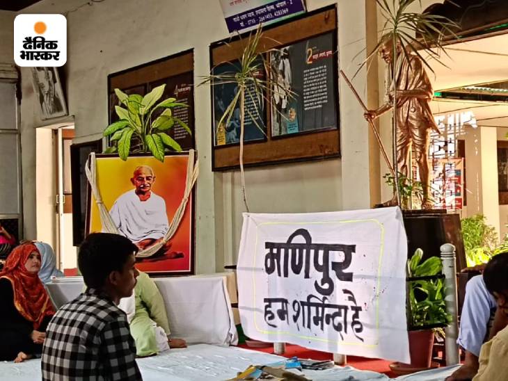 महात्मा गांधी की प्रतिमा के सामने बैठे लोग।