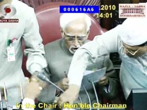 8 मार्च 2010 को राज्यसभा के सभापति हामिद अंसारी की टेबल से महिला आरक्षण विधेयक की कॉपी खींचने और माइक तोड़ने की कोशिश करते सांसद। ये तस्वीर राज्यसभा टीवी के प्रसारण के दौरान लिया गया स्क्रीनशॉट है।