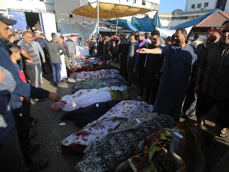 गाजा शहर के अल-शिफा अस्पताल में कफन में लिपटे शवों के आसपास शोक मनाते लोग।