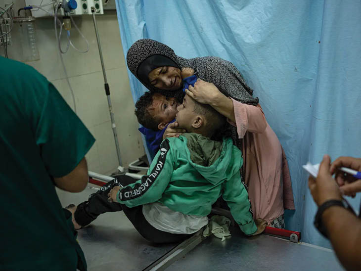 गाजा के अस्पताल में एक मां घायल बच्चों के साथ इलाज मिलने का इंतजार करती नजर आई।