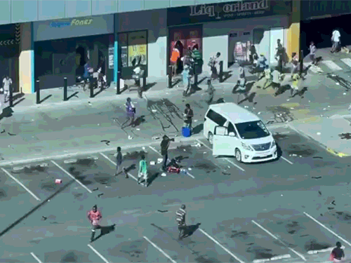 पोर्ट मोरेस्बी के एक शॉपिंग कॉम्प्लेक्स के बाहर लोगों की भीड़ को चुराया हुआ सामान ले जाते हुए देखा जा सकता है।