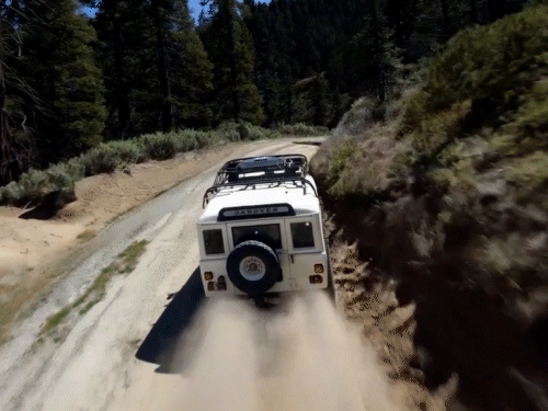 Prompt: The camera follows behind a white vintage SUV with a black roof rack as it speeds up a steep dirt road surrounded by pine trees on a steep mountain slope, dust kicks up from it’s tires, the sunlight shines on the SUV as it speeds along the dirt road, casting a warm glow over the scene. The dirt road curves gently into the distance, with no other cars or vehicles in sight. The trees on either side of the road are redwoods, with patches of greenery scattered throughout. The car is seen from the rear following the curve with ease, making it seem as if it is on a rugged drive through the rugged terrain. The dirt road itself is surrounded by steep hills and mountains, with a clear blue sky above with wispy clouds.