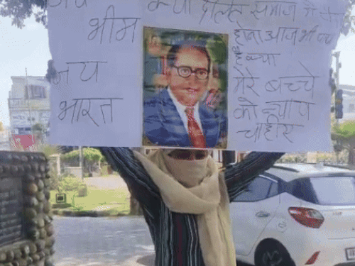 बाबा साहब भीमराव अंबेडकर का बैनर लेकर धरना देती पीड़िता।