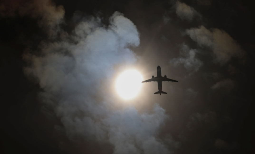 न्यू यॉर्क के क्वींस में आंशिक सूर्य ग्रहण के दौरान आसमान में उड़ता प्लेन।