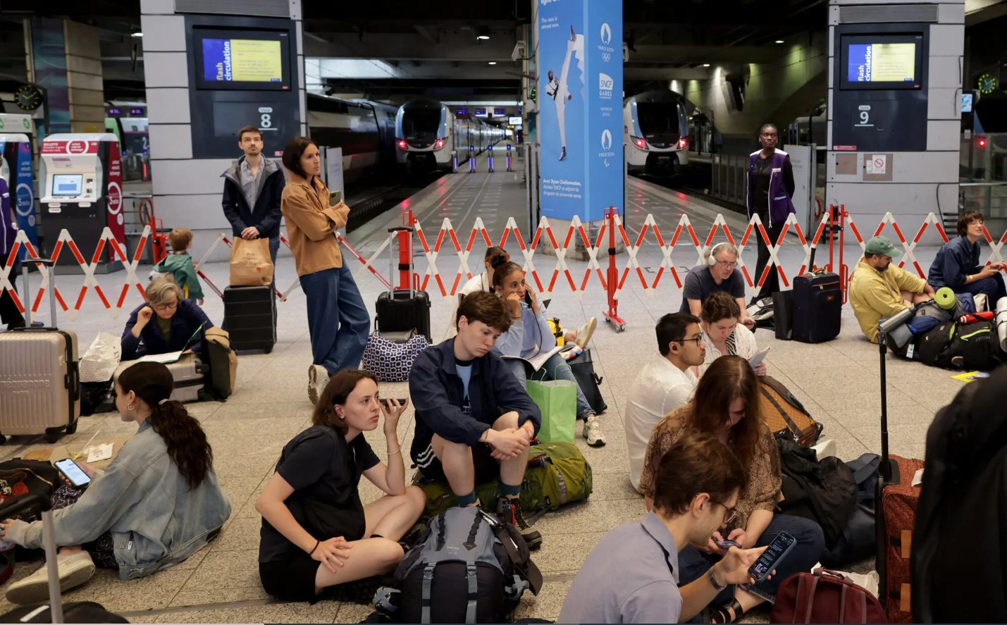 गा मॉनपानास स्टेशन पर यात्री ट्रेनों के इंतजार में जमीन पर बैठे नजर आए।