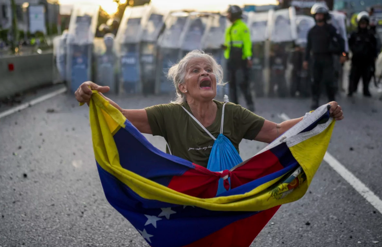 An elderly woman protesting against the government with the Venezuelan flag.