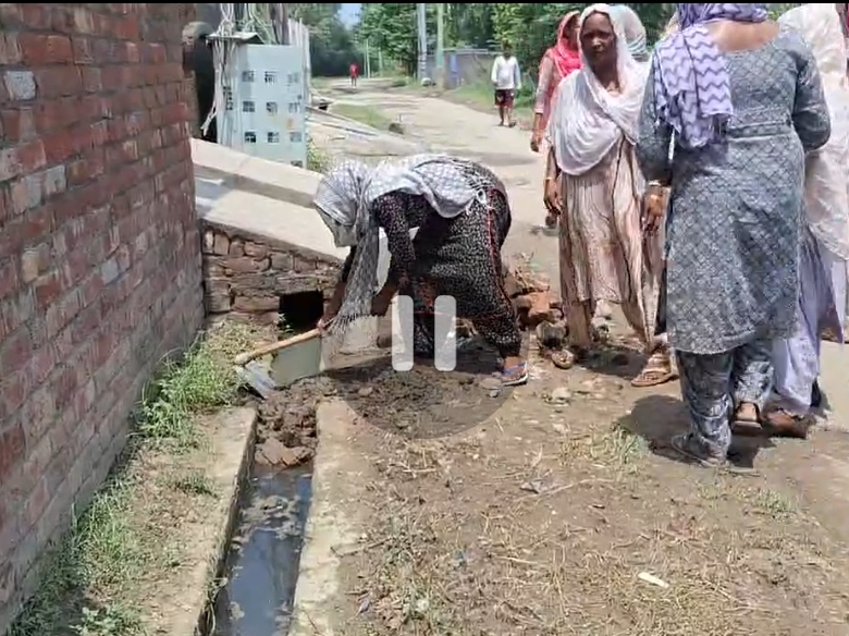नाली से मलबा निकालते हुए महिला।