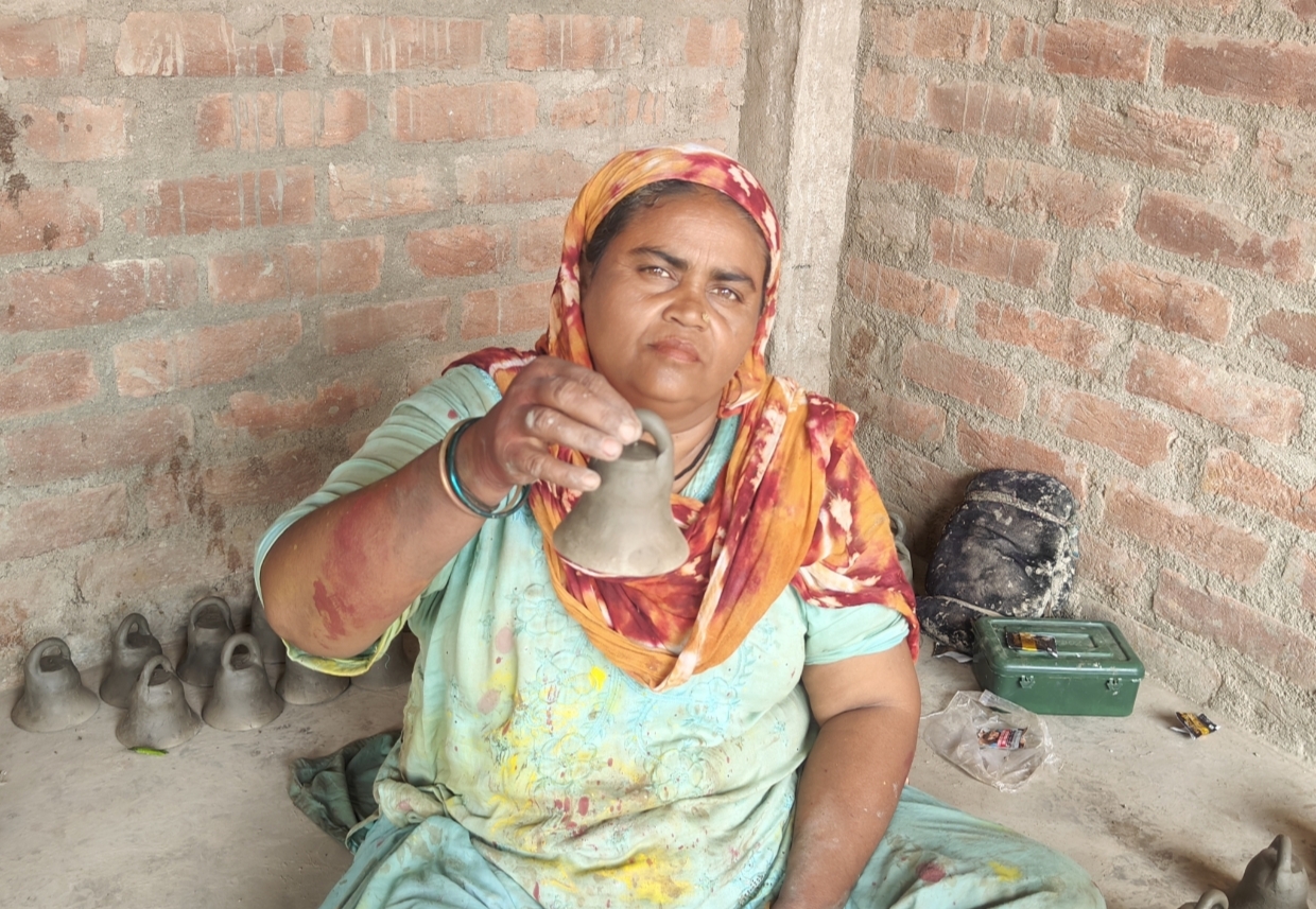 मिट्टी से बनाई गई घंटी को दिखाती हुई परिवार की सदस्य।