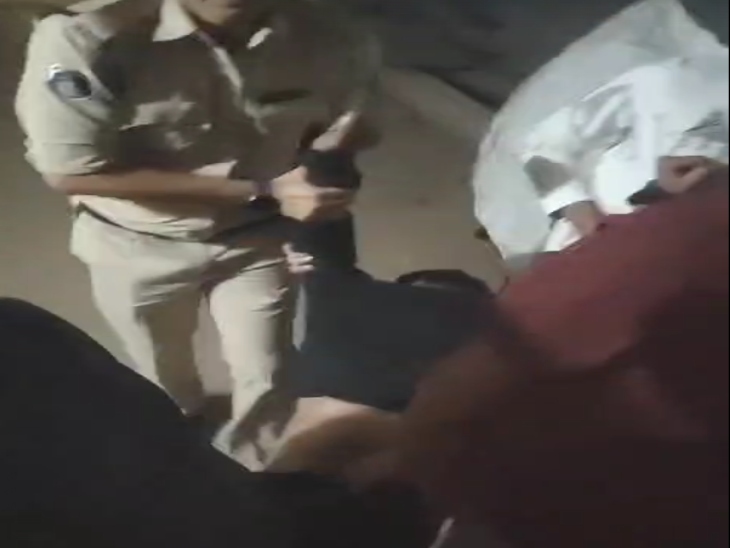 पुलिसकर्मी बदमाश को हाथ और पैरों से पकड़ कर गाड़ी में ले जा रहे हैं।