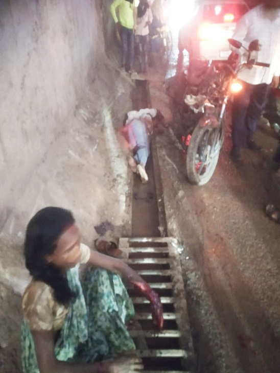 पति के पास बैठी घायल पत्नी और खड़े लोग।