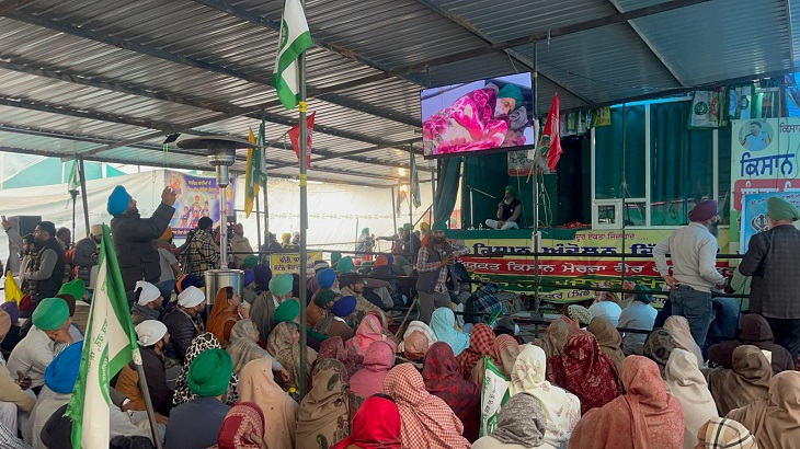 People sitting on hunger strike at Khanauri border watching Dallewal on the screen.