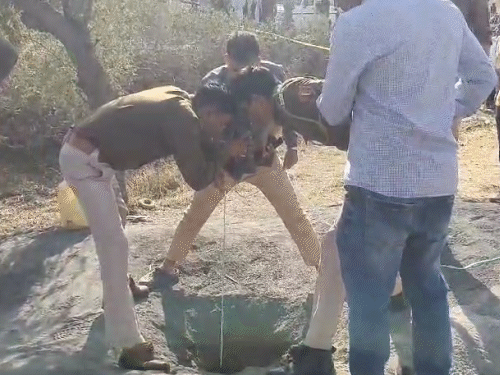 टॉर्च की मदद से बोरवेल में बच्चे को देखने की कोशिश करते पुलिसकर्मी।