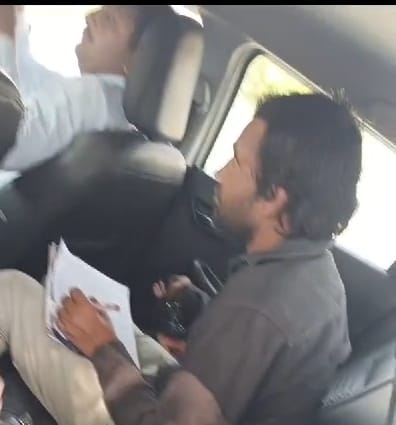 परीक्षा केंद्र के बाहर गाड़ी में बैठकर नकल की पर्चियां तैयार करते युवक