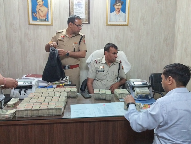 सूरजकुंड थाना इलाके में गाड़ी से पकड़े गए कैश को मशीन की मदद से गिनते पुलिस कर्मचारी