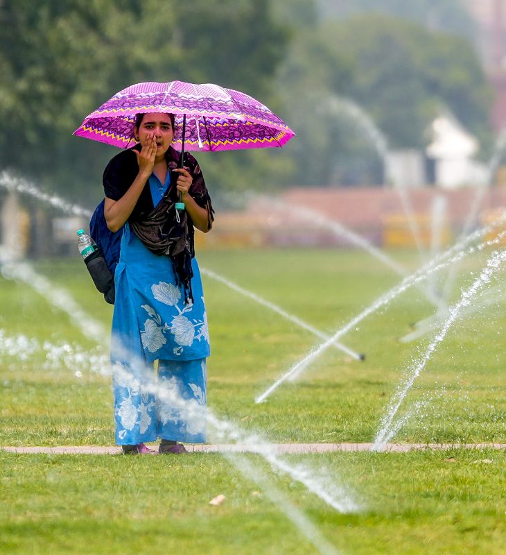 दिल्ली के कर्तव्य पथ के किनारे चिलचिलाती धूप से खुद को बचाने के लिए छाता लिए एक युवती पानी के फव्वारे से मुंह पोंछती दिखी।