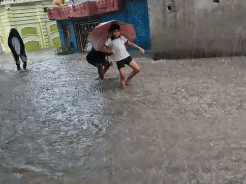 बच्चे छाता लेकर पानी में उतरे है।