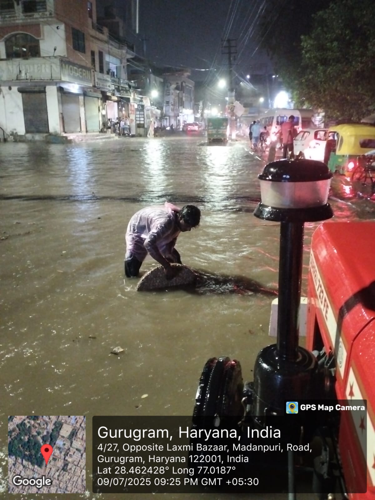 गुरुग्राम में रात के समय मदनपुरी रोड पर सीवर के ढक्कन हटाकर पानी की निकासी करवाता नगर निगम कर्मी।