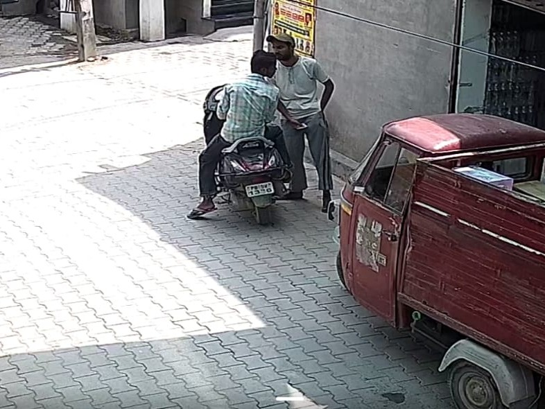 दुकान के बाहर स्कूटी पर खड़े दो युवक।