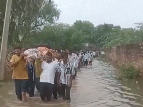 नागौर की खींवसर ग्राम पंचायत में मंगलवार को घुटनों तक भरे पानी में से अर्थी को श्मशान ले जाते लोग।
