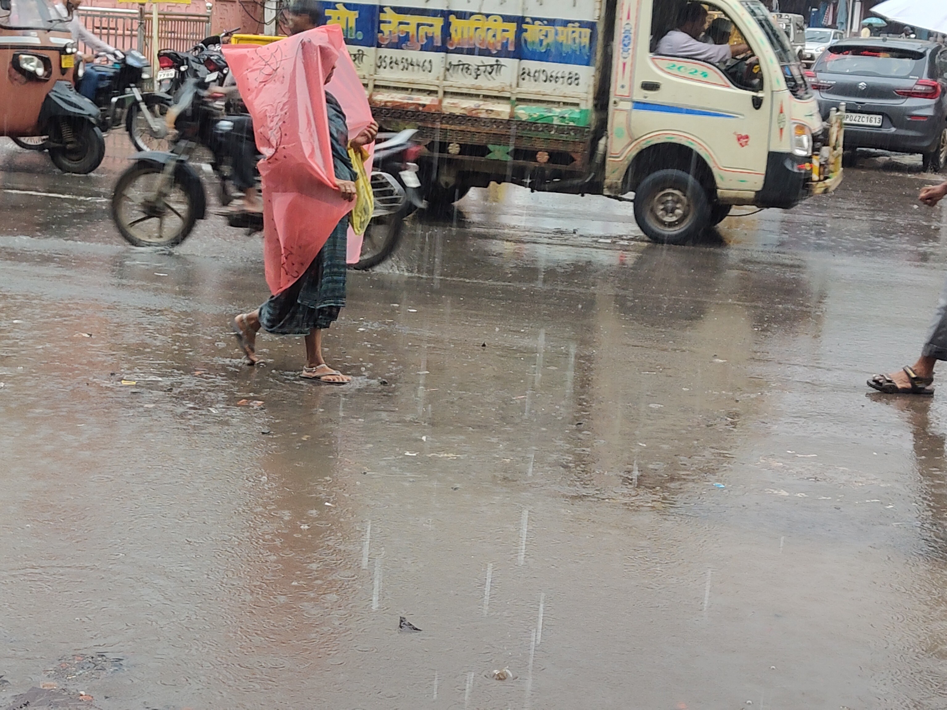 बारिश के बीच खुद को पानी से बचाने की कोशिश करते लोग।