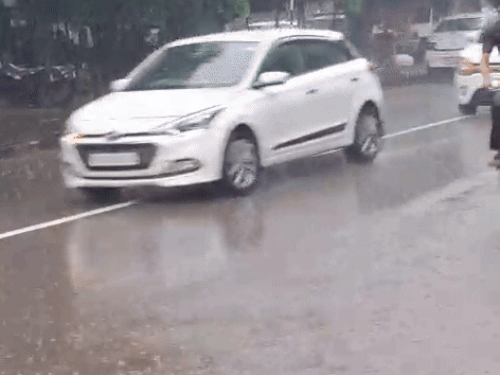 बारिश में भीगते हुए साइकिल में पर जाते हुए व्यक्ति व अन्य वाहन।