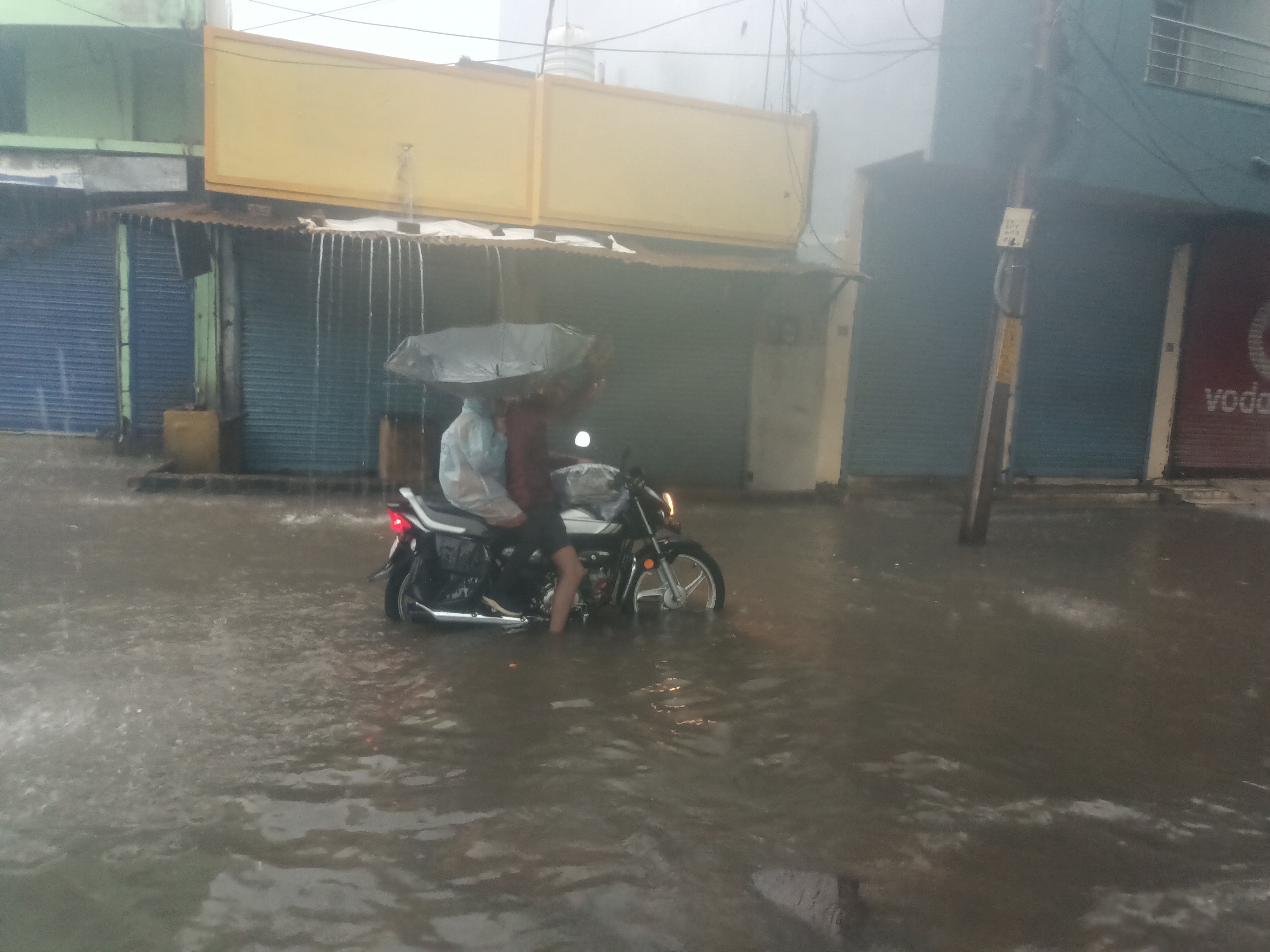 बारिश और पानी से भरे सड़क के बीच फंसे बाइक सवार