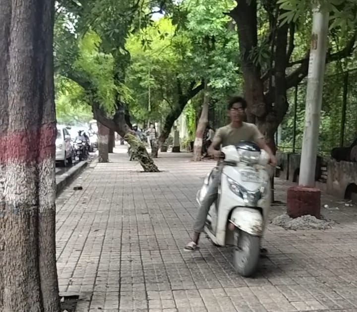 फुटपाथ पर स्कूटी दौड़ाता युवक