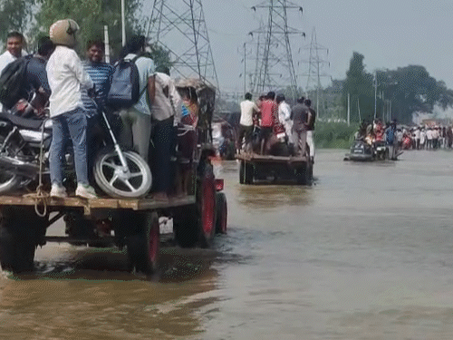 यूपी के बिजनौर में सड़कों पर कमर तक पानी भरा, ट्रैक्टर के जरिए रास्ता पार करते लोग।