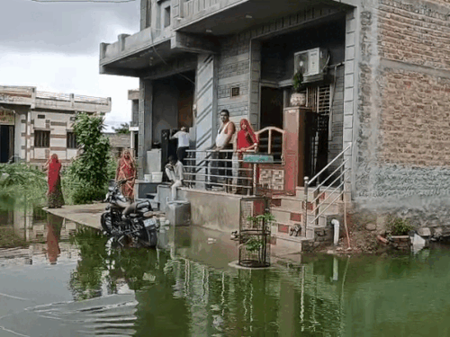 घर के चारों और भरा तालाब का पानी, मकान गिरने के डर से बाहर बैठे परिवार के लोग