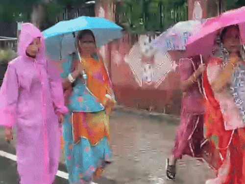 अजमेर के वैशाली नगर चौपाटी के पास बरसात के दौरान छाता लेकर निकली महिलाएं।