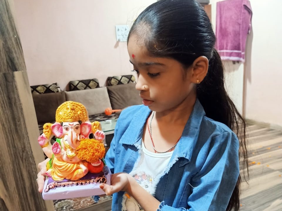 बच्ची ने थामी गणेश जी की प्रतिमा, चेहरे पर दिखा उत्साह।